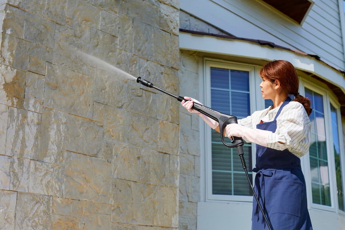 Technician soft washing a stone exterior wall of a home